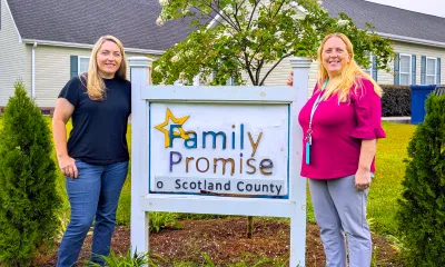 Tina and Kristy stand beside Family Promise sign.