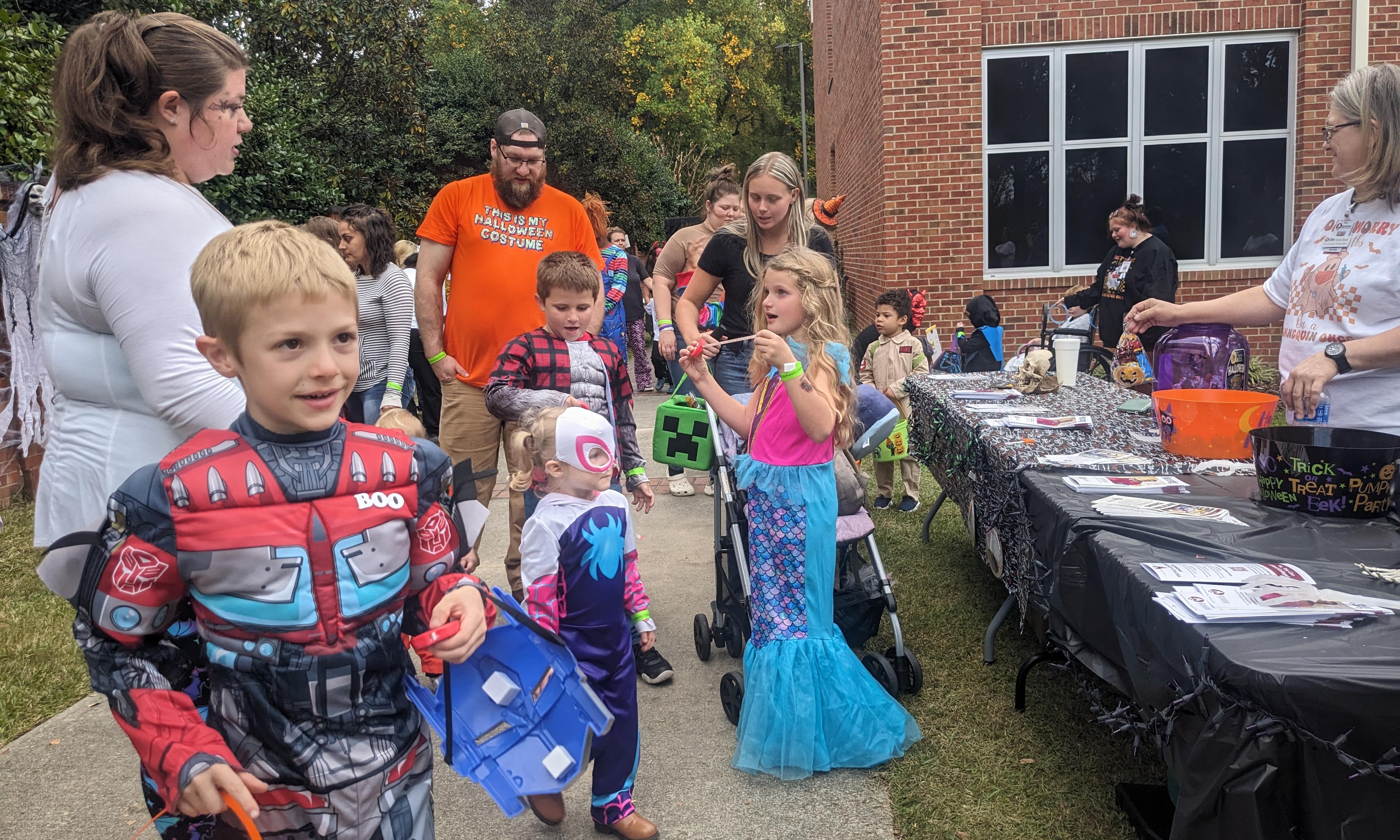 Kids in costumes line up to get candy from a table behind the Grimsley Building at the 2024 Trick or Treat to the Trail