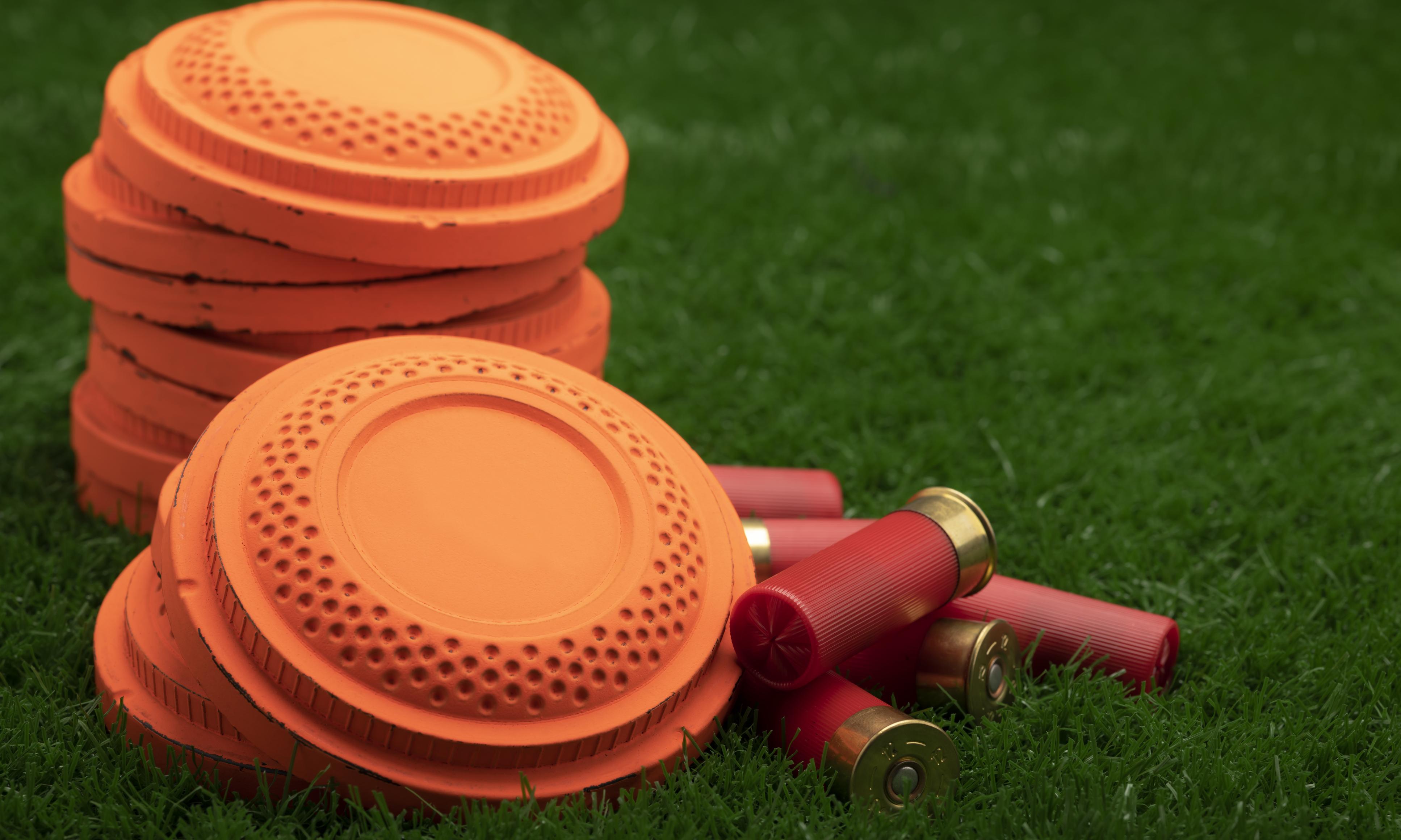 Photo of orange clay pigeons and shotgun shells in the grass